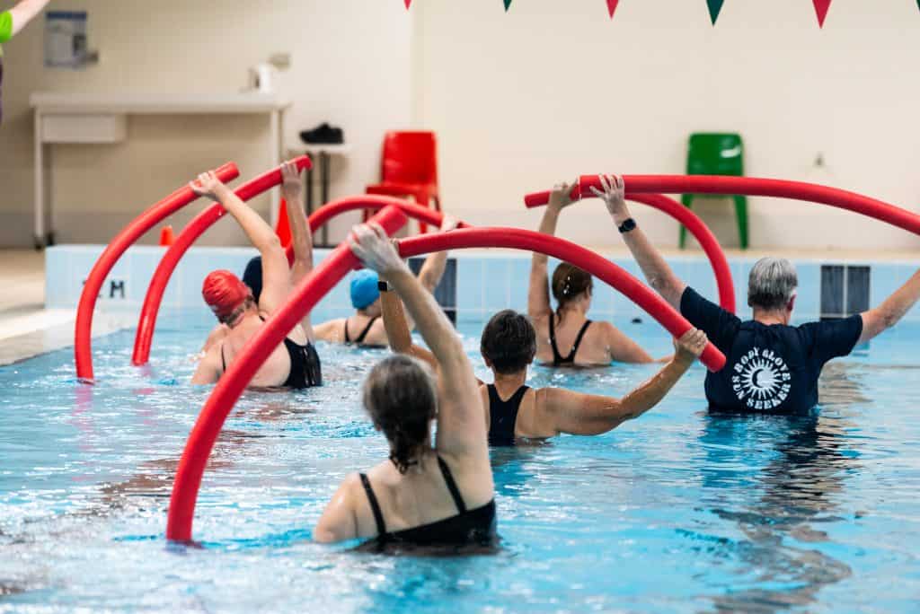 Women in pool with red pool noodles performing water running exercises